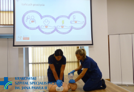 Pracownicy szpitala prezentują przeprowadzanie pierwszej pomocy na manekinie na ekranie widoczny łańczuch przeżycia