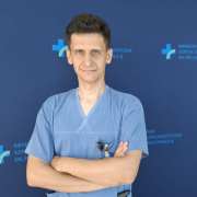 Dr Łukasz Niewiara na tle szpitalnych logotypów.