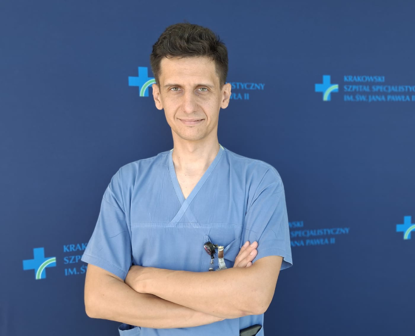 Dr Łukasz Niewiara na tle szpitalnych logotypów.