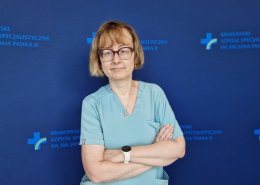 Lek. Górkiewucz-Kot na tle granatowej ścianki z logotypami szpitala.