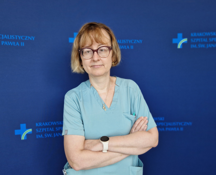 Lek. Górkiewucz-Kot na tle granatowej ścianki z logotypami szpitala.