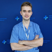 mgr Miłosz Wujek w medycznym ubraniu na granatowym tle