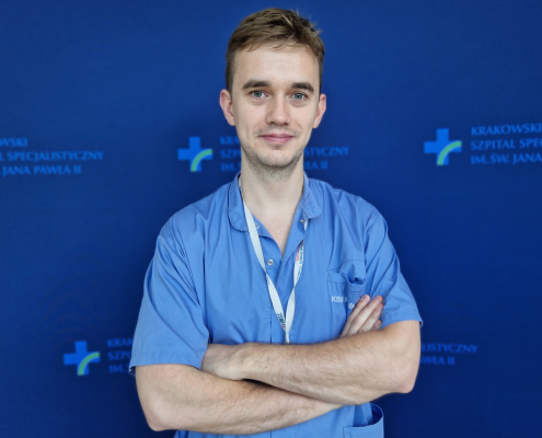 mgr Miłosz Wujek w medycznym ubraniu na granatowym tle