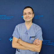 dr n. med. Adam Mazurek na granatowym tle w ubraniu medycznym