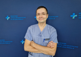 dr n. med. Adam Mazurek na granatowym tle w ubraniu medycznym