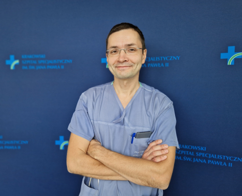 dr n. med. Adam Mazurek na granatowym tle w ubraniu medycznym