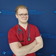 lek. Mateusz Winiarczyk na granatowym tle w medycznym ubraniu