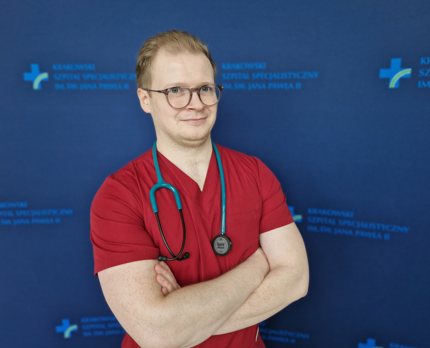 lek. Mateusz Winiarczyk na granatowym tle w medycznym ubraniu