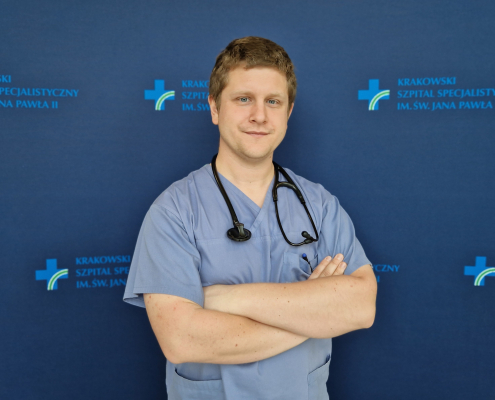 lek. Łukasz Wilczek w medycznym ubraniu na granatowym tle