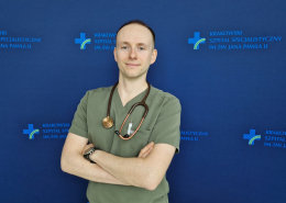 lek. Michał Surdacki w medycznym ubraniu na granatowym tle