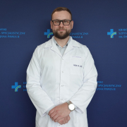 Dr n. med. Krzysztof Krawczyk w medycznym ubraniu na granatowej ściance