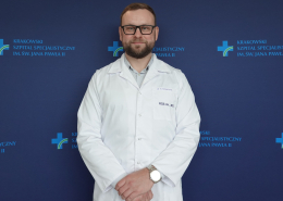 Dr n. med. Krzysztof Krawczyk w medycznym ubraniu na granatowej ściance
