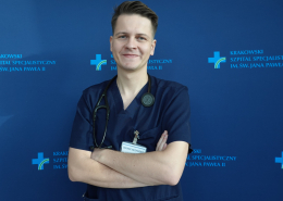 lek. Krystian Mróz w medycznym ubraniu na granatowym tle