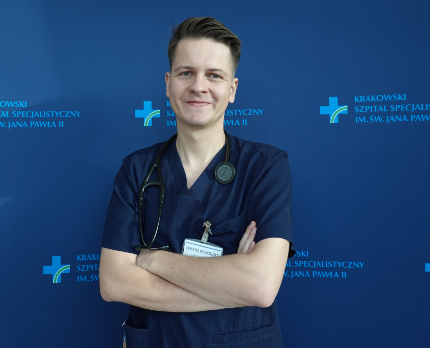 lek. Krystian Mróz w medycznym ubraniu na granatowym tle