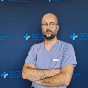 Lek. Krzysztof Karwat w medycznym ubraniu na granatowym tle