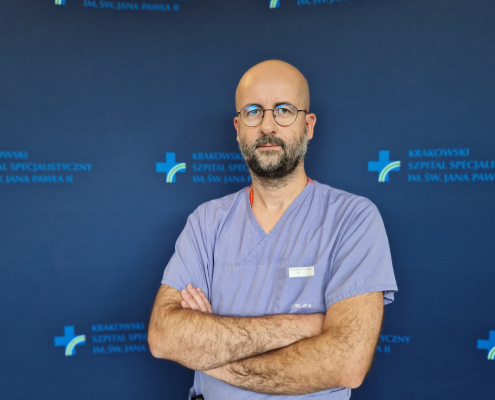 Lek. Krzysztof Karwat w medycznym ubraniu na granatowym tle