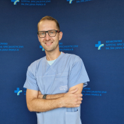 dr med. Mateusz Podolec w medycznym ubraniu na granatowej ścianie