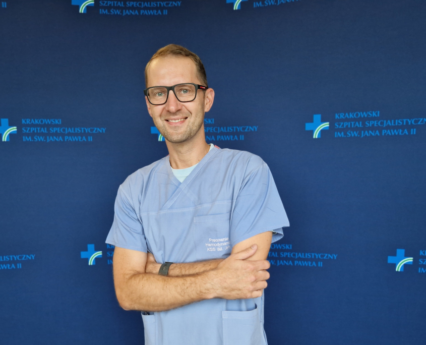 dr med. Mateusz Podolec w medycznym ubraniu na granatowej ścianie