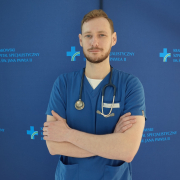 lek. med. Maciej Pawluś w medycznym ubraniu na granatowym tle