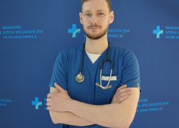 lek. med. Maciej Pawluś w medycznym ubraniu na granatowym tle