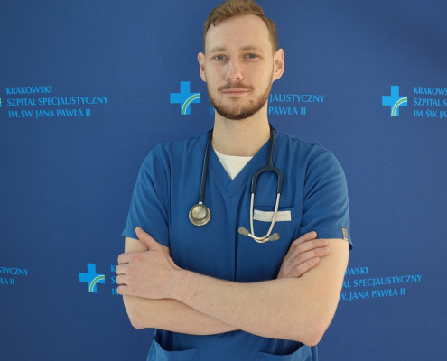 lek. med. Maciej Pawluś w medycznym ubraniu na granatowym tle