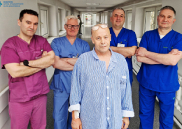 Zespół przeprowadzający zabieg - 4 lekarzy i pacjent na szpitalnym korytarzu.