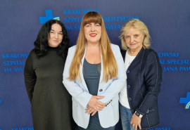 Prof. Komar, Dr Holcman i prof. Kostkiewicz na ściance w kolorze granatowym z logotypami Szpitala.
