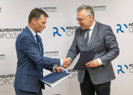 Prorektor ds. Ogólnych Politechniki Opolskiej wraz z Dyrektorem Szpitala lek. Grzegorzem Fitasem podczas podpisywania umowy o współpracy na tle ścianki z logotypami Politechniki Opolskiej.