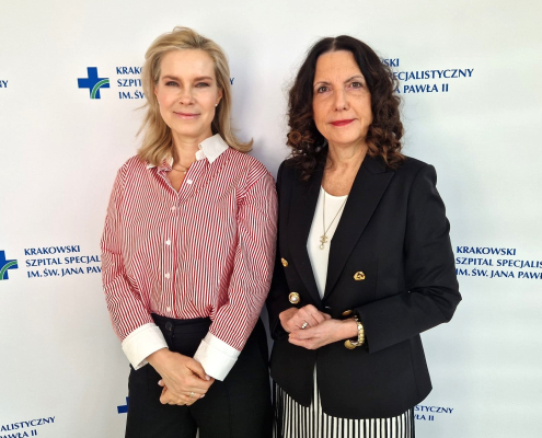 prof. Joanna Natorska wraz z prof. Anetta Undas na tle białej ścianki z logotypem szpitala.